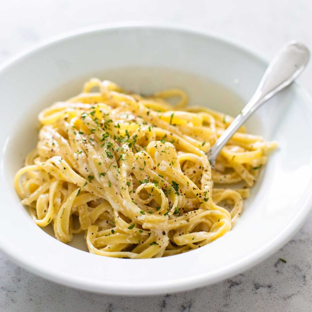A white bowl is filled with fettuccine alfredo with a fork.
