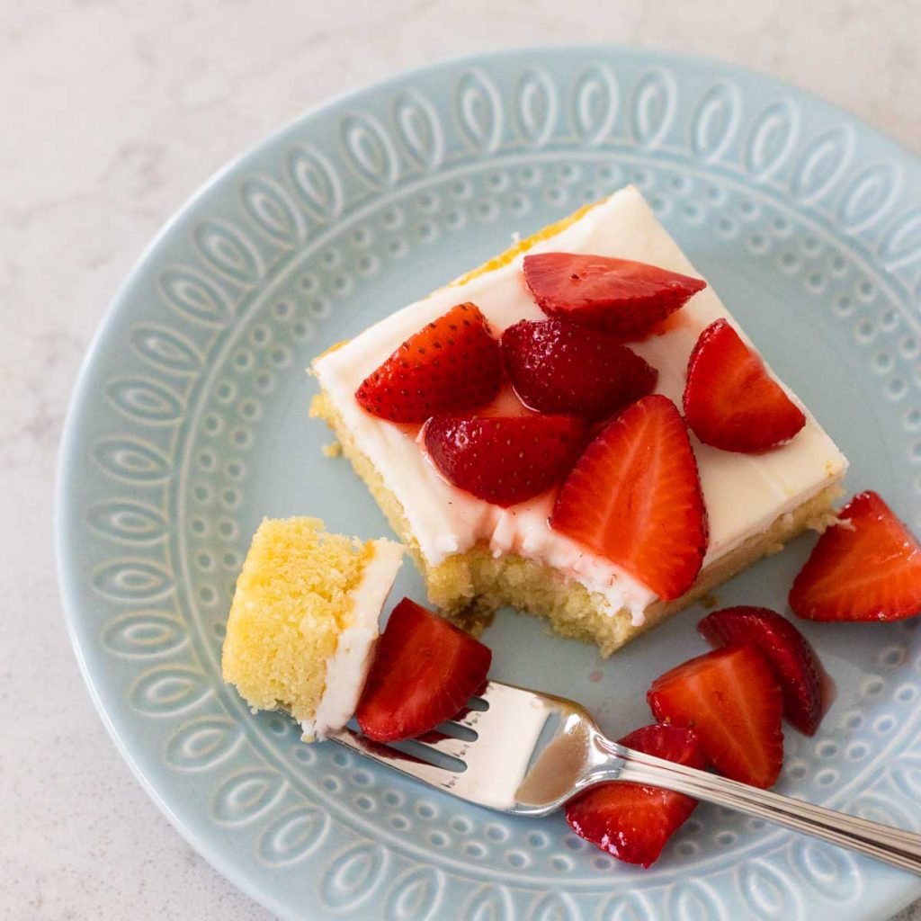 A square slice of almond cake with almond icing has fresh strawberries sprinkled over the top.