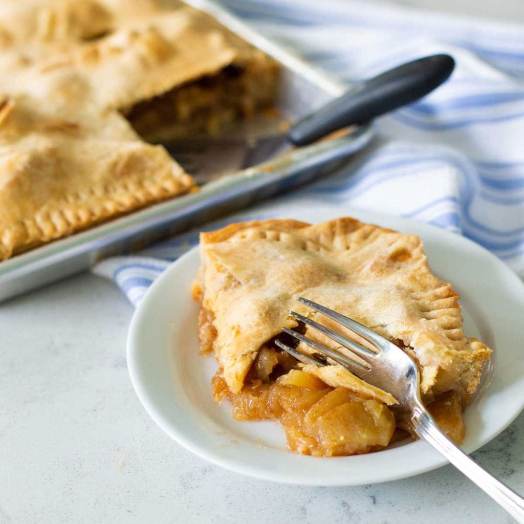 A classic apple pie has been served on a white plate with a fork.
