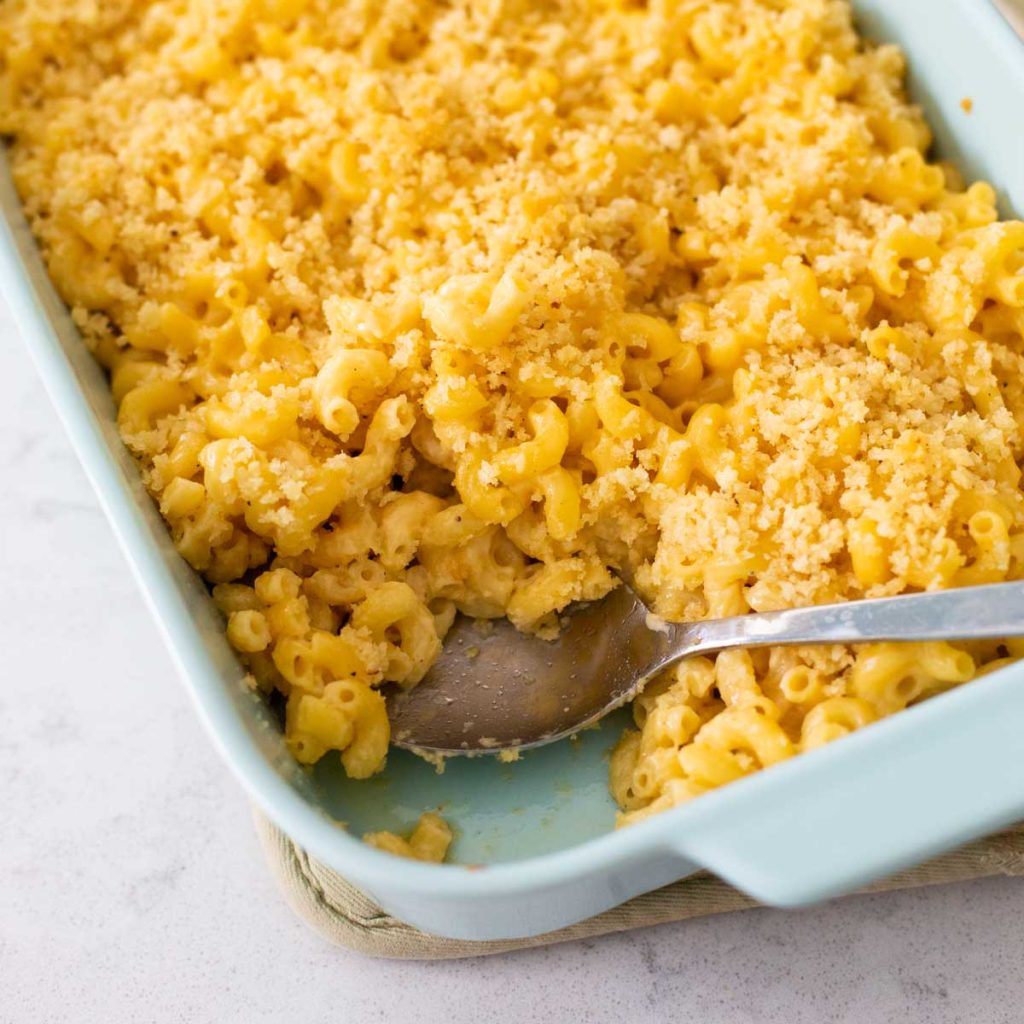 A baked mac and cheese casserole with bread crumbs on top is in a blue baking dish with a spoon.