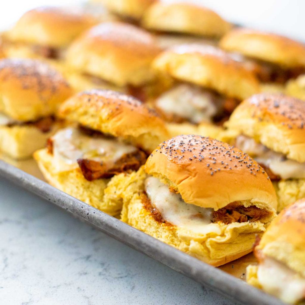 A pan of bbq chicken sliders with melted cheese peeking out from the buns.