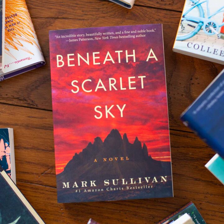 A copy of the book Beneath a Scarlet Sky is on the table.