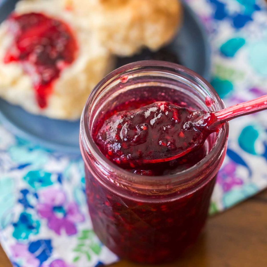 A mason jar filled with jam sits in front of a biscuit.