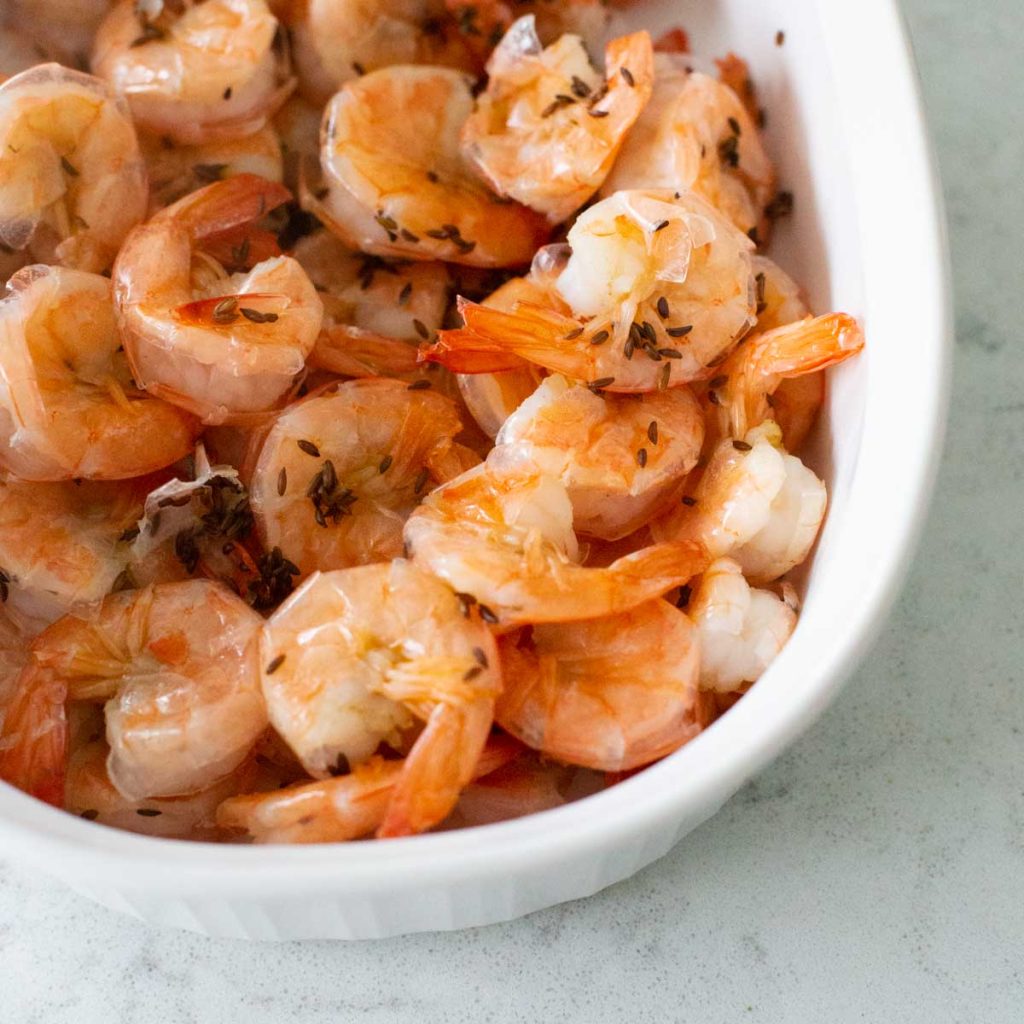 A white dish is filled with boiled shrimp and caraway seeds.