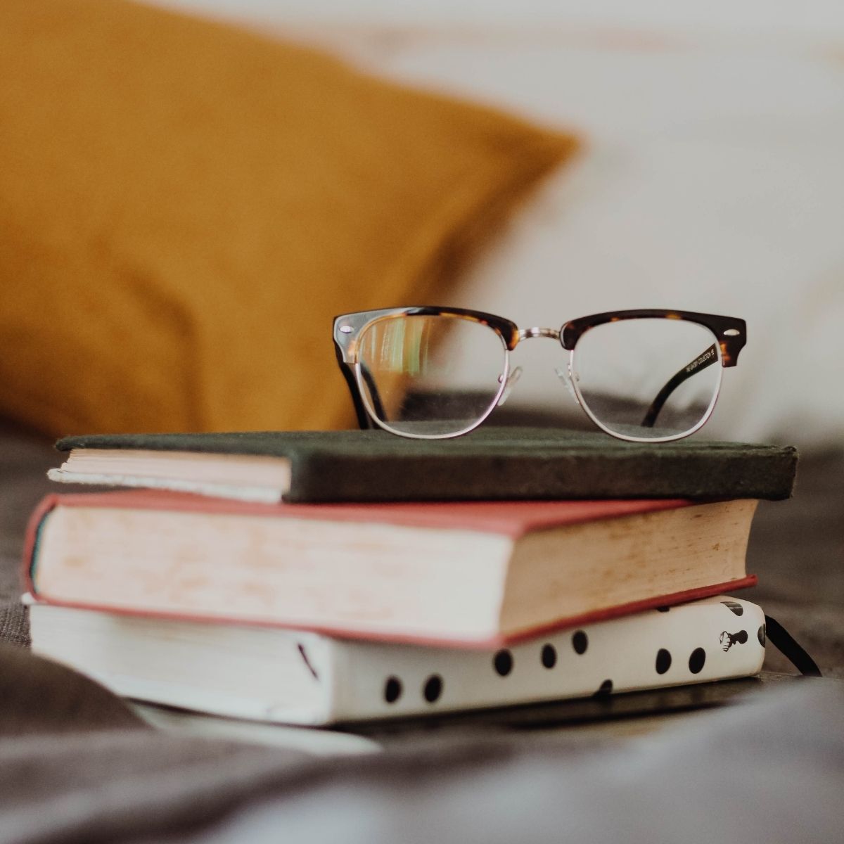 A stack of books with a pair of glasses on top.