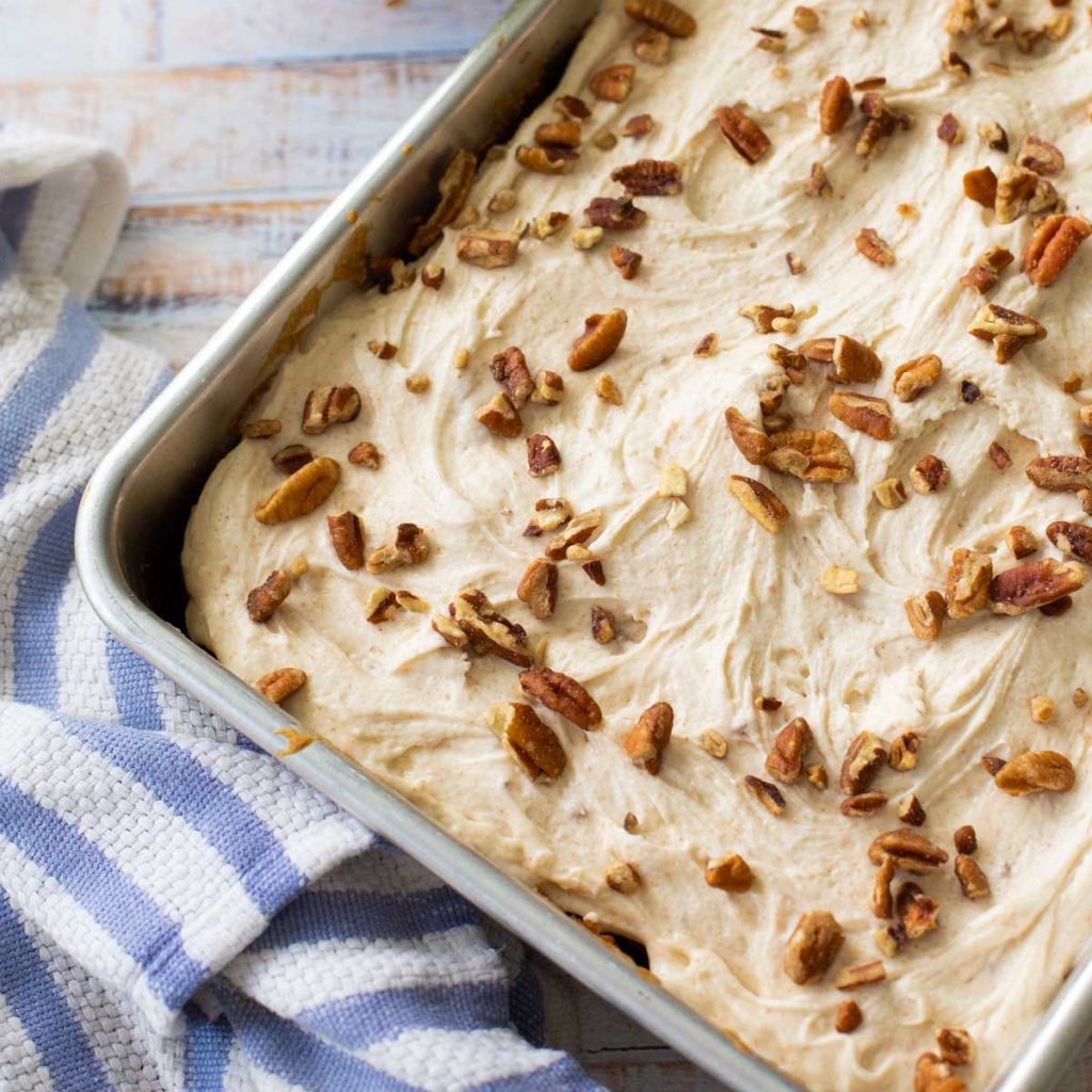 A baking pan has a cake frosted with brown butter frosting and chopped pecans.