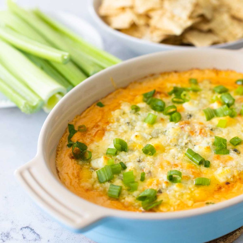 A baking dish of hot buffalo chicken dip has celery and chips in the background.
