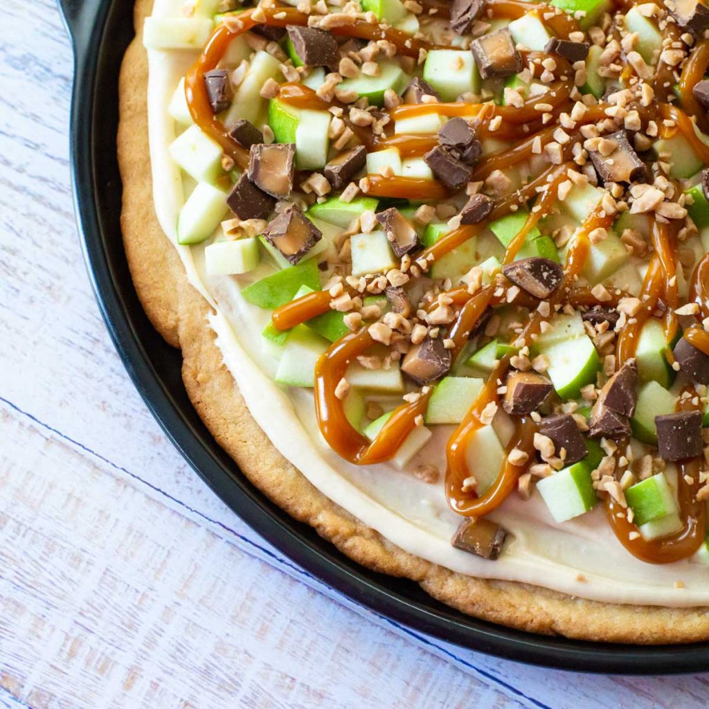 A caramel apple sugar cookie pizza with fresh apples and Snickers candy.