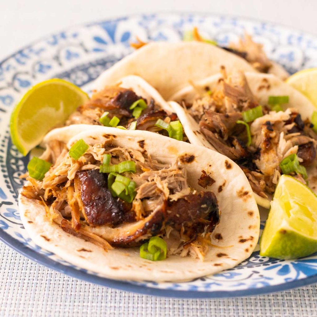 A plate of carnitas tacos with fresh lime wedges.