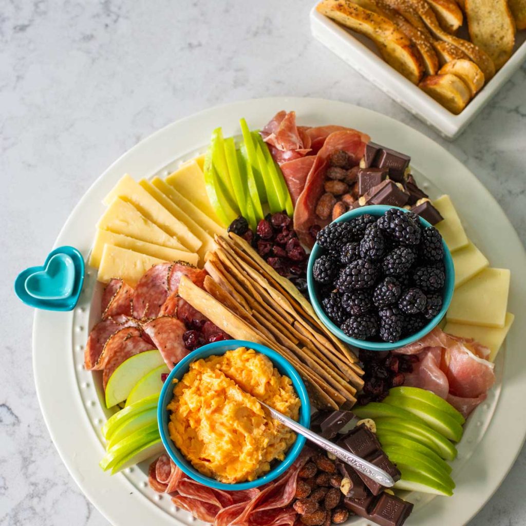 A charcuterie board with cheeses, meats, and blackberries and apple slices.