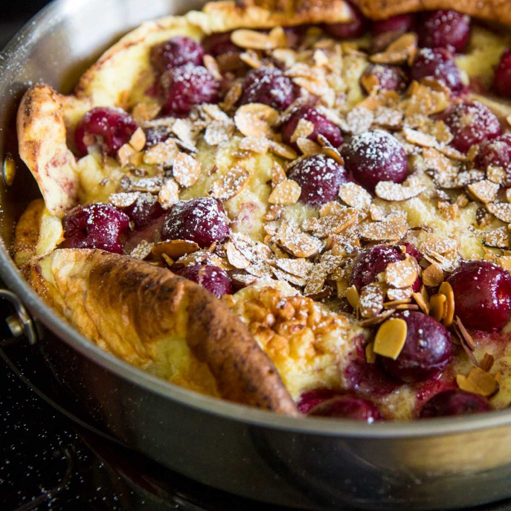 A Dutch Baby cherry pancake is puffy at the edges and has toasted almonds over the top.