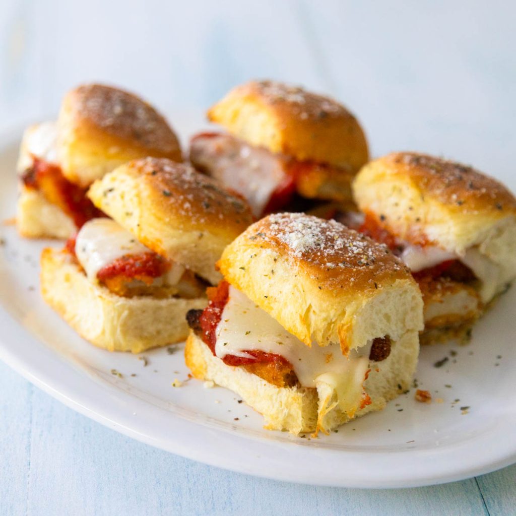 A white platter of chicken parm sliders shows the melted cheese coming from inside.