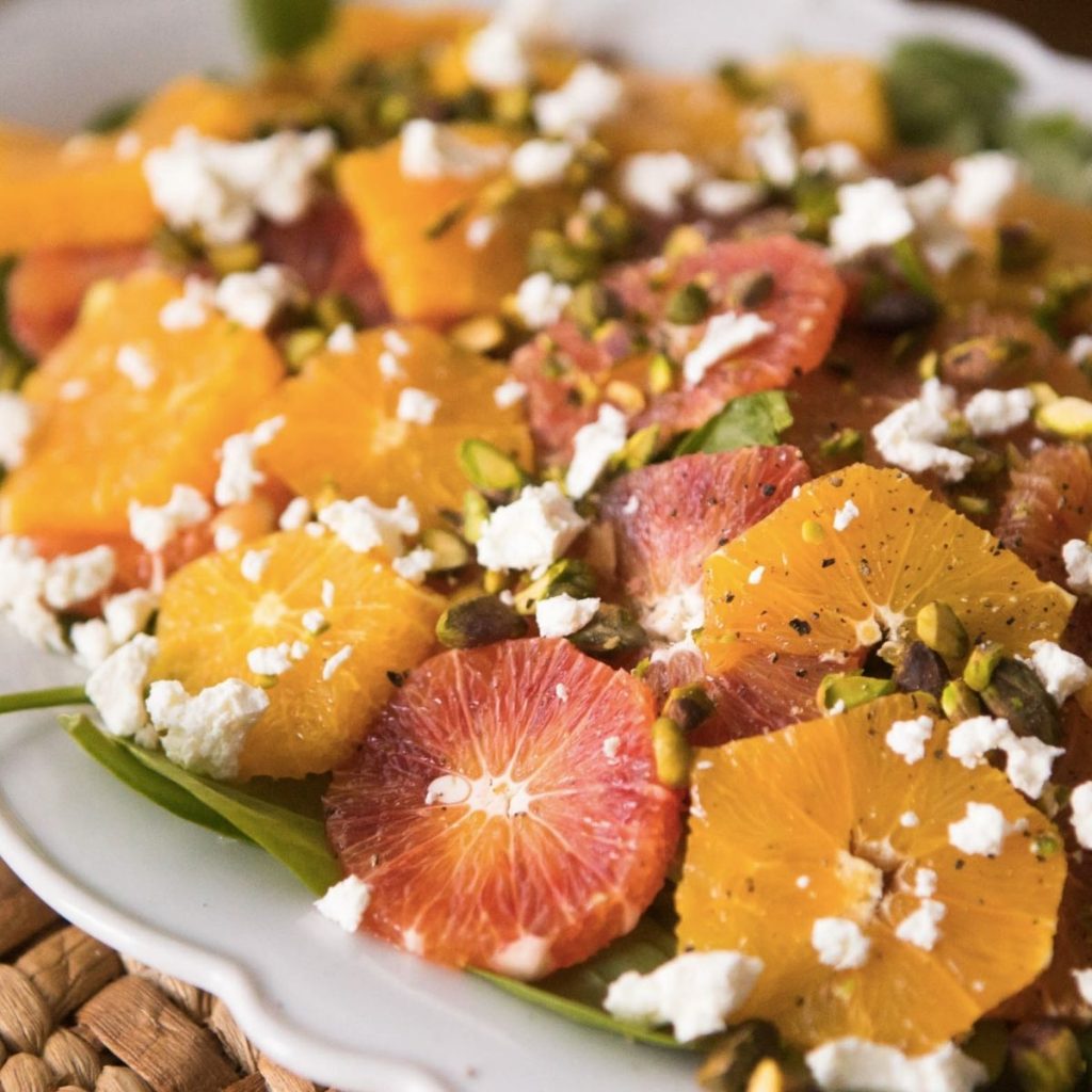 A white platter is filled with sliced orange and grapefruits sprinkled with goat cheese.