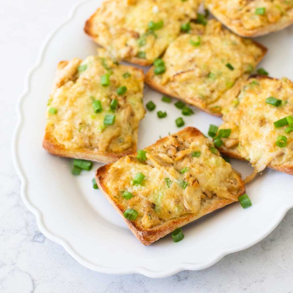 A white ruffled platter with cheesy crab melts are served with fresh green onions.