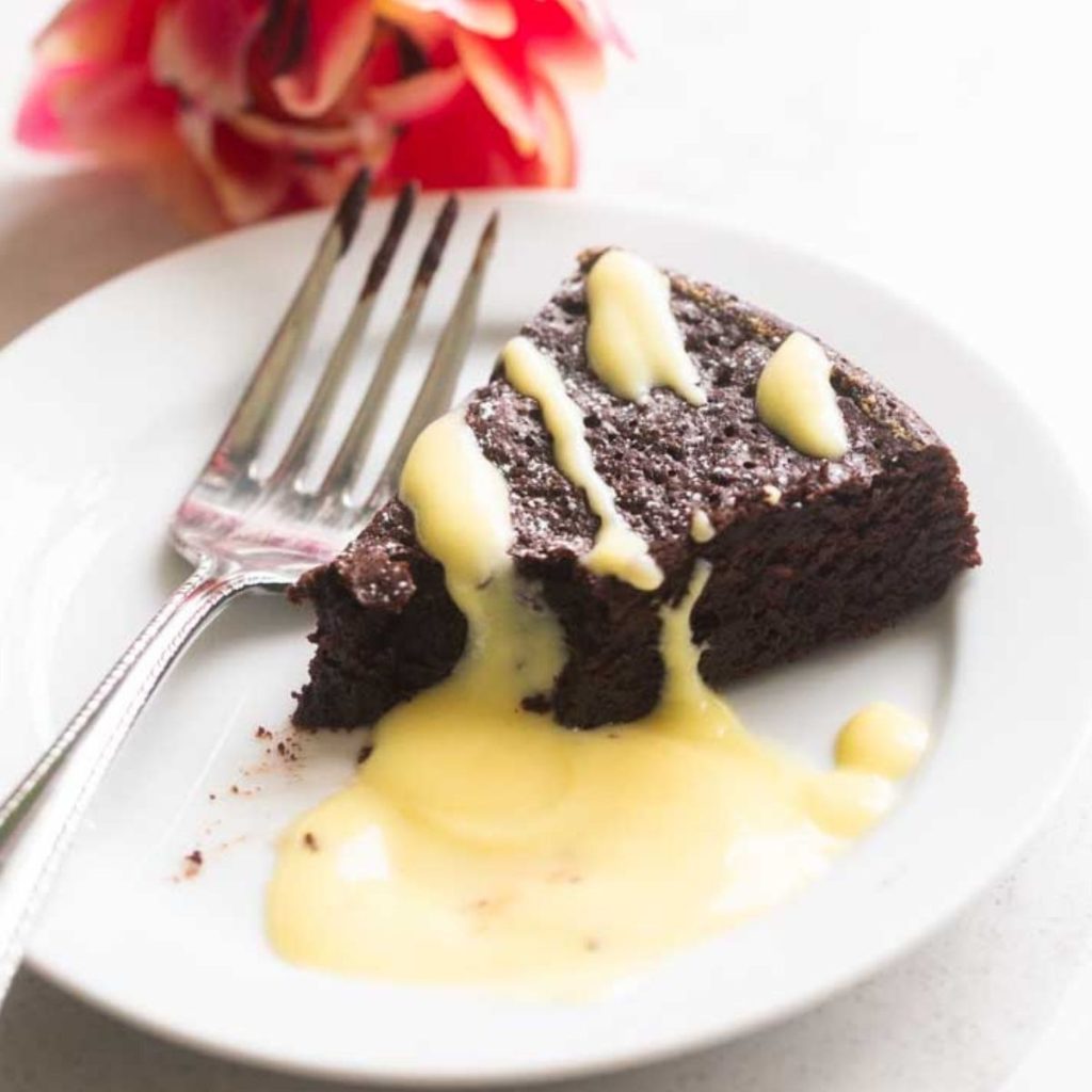 A slice of chocolate fudge cake has a drizzle of vanilla sauce over the top.
