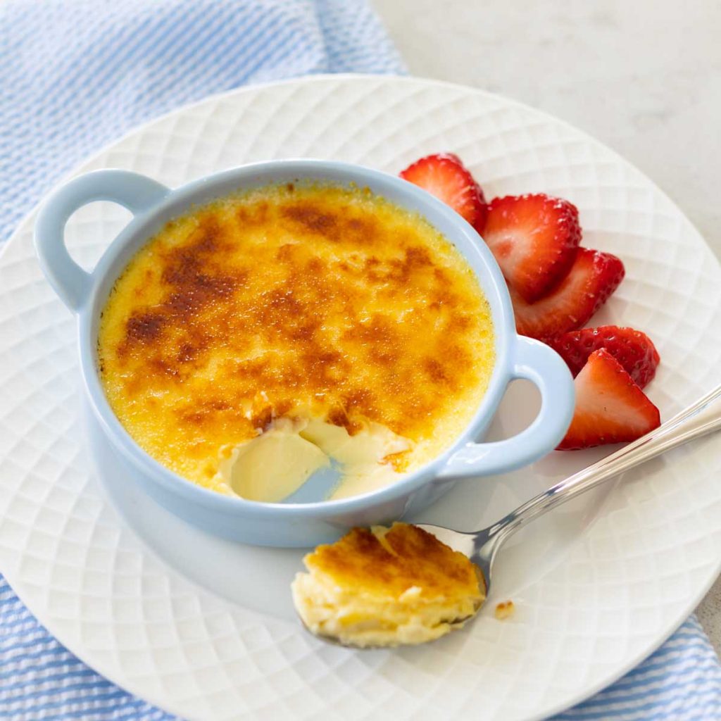 A blue dish of creme brulee has fresh strawberries on the side.