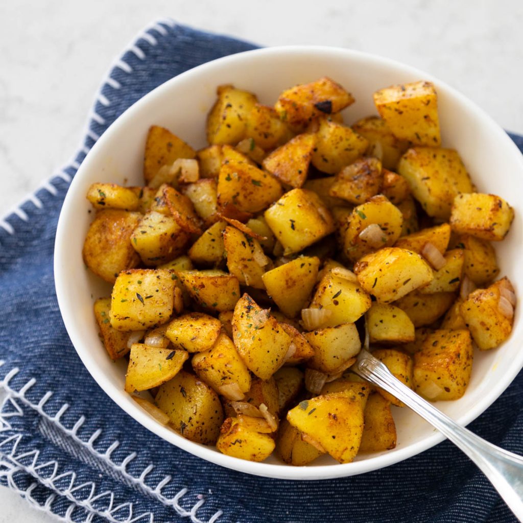 A white bowl filled with home fries.