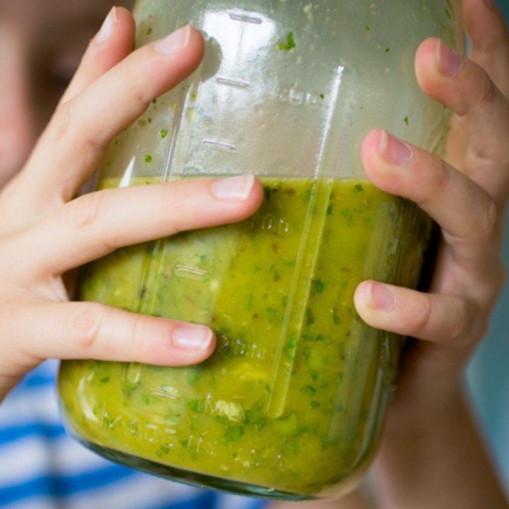 A girl shakes a mason jar filled with a green Cuban mojo marinade.