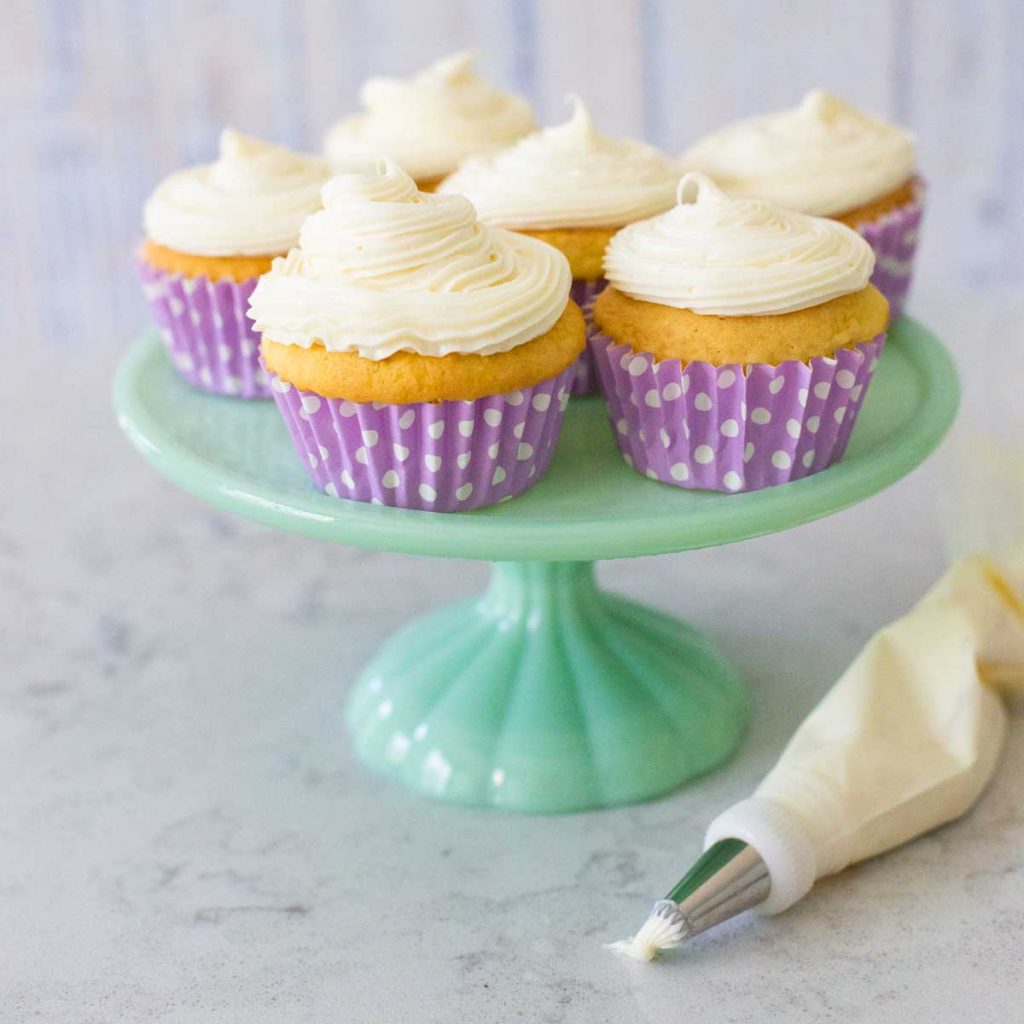 A batch of vanilla cupcakes have cream cheese frosting on them.
