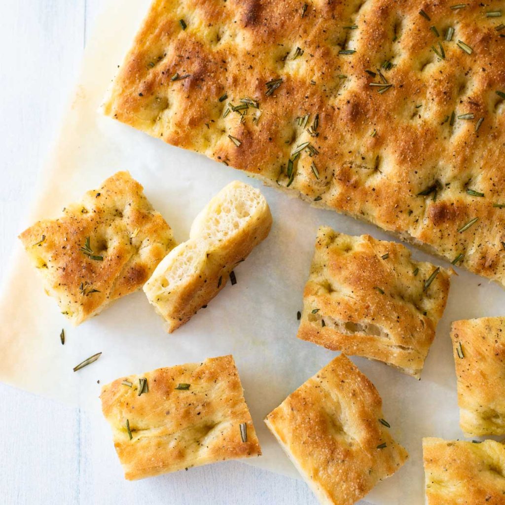 A baked Italian style flatbread has been sliced into squares on a piece of parchment paper.