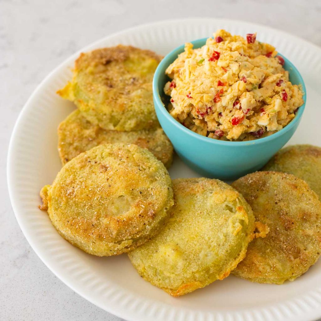 A platter of fried green tomatoes has a bowl of pimento cheese on top.