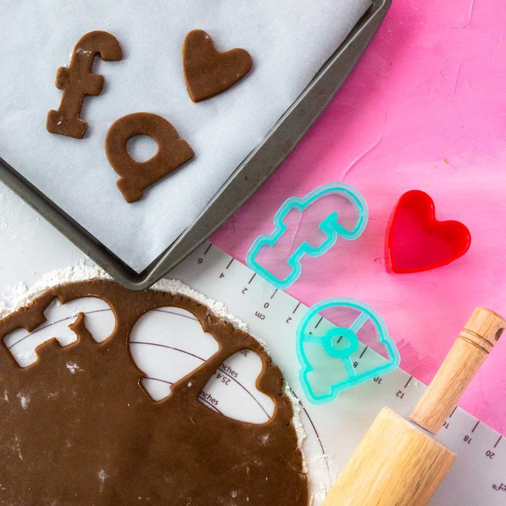 Gingerbread cookie dough has been rolled out and cut with letter-shaped cookie cutters to spell "fa" for fa la la.