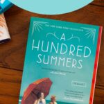 A copy of the book A Hundred Summers sits on a table.