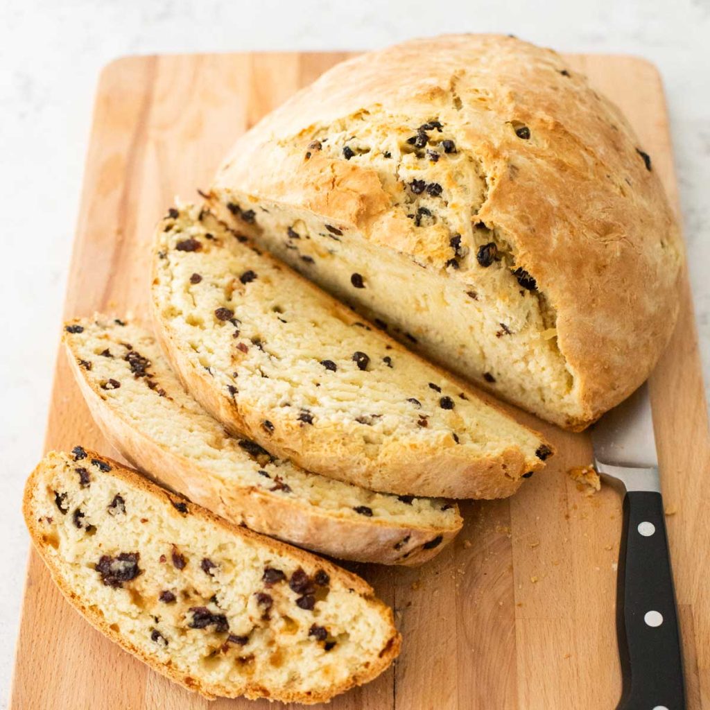 A loaf of irish soda bread has been sliced with a knife to show the raisins inside.