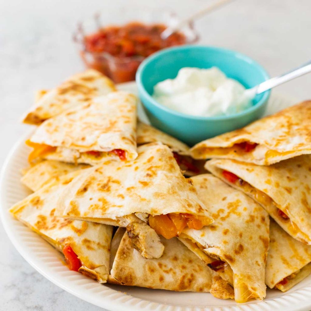 A platter of quesadillas with sour cream and salsa.