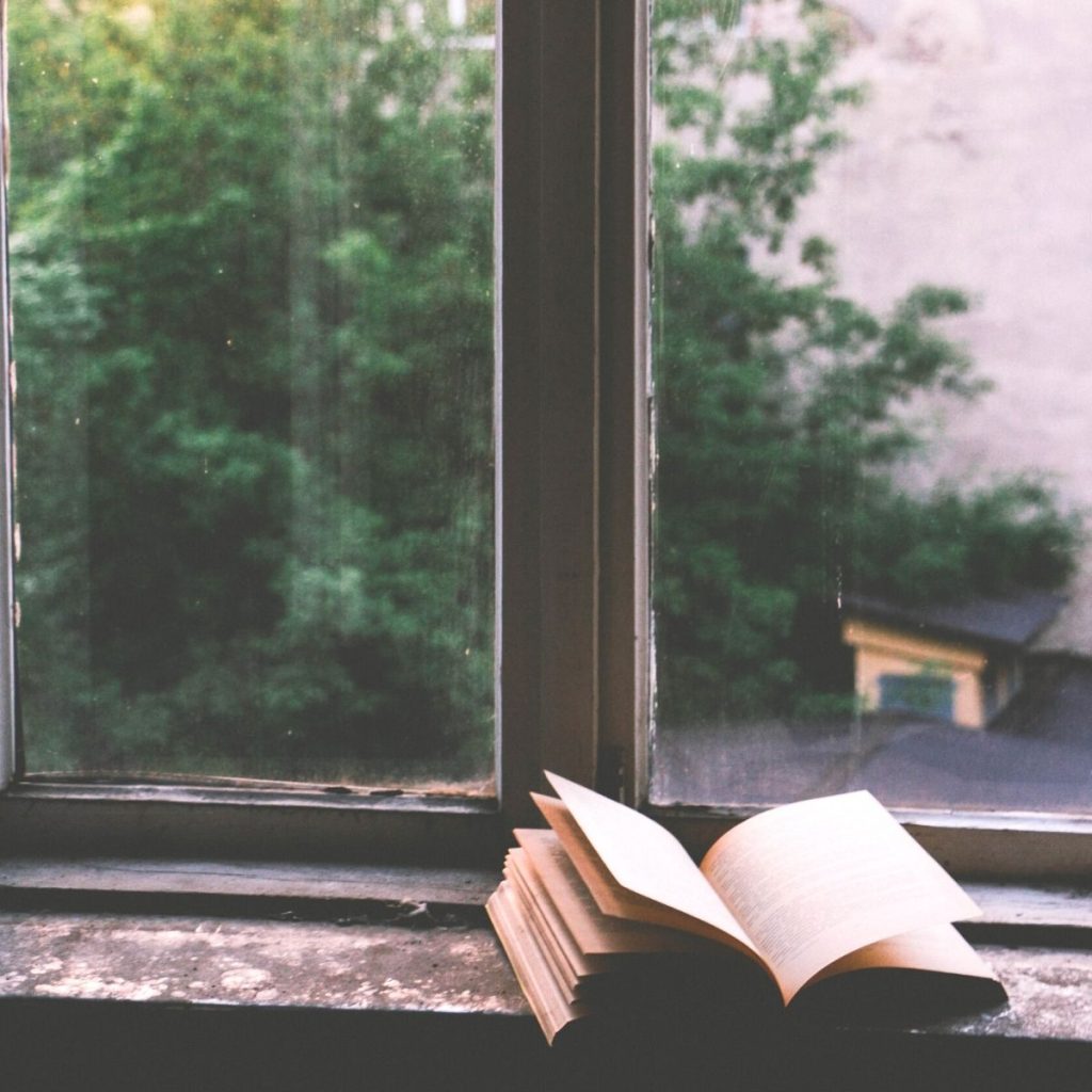 An open book sits in a window sill with the light streaming in.
