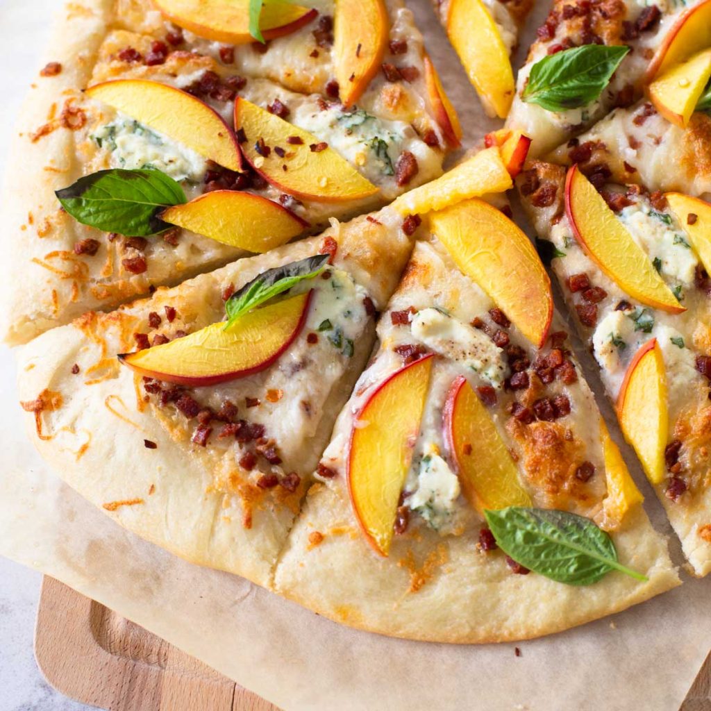 A pizza with fresh peaches and basil has been sliced to serve.