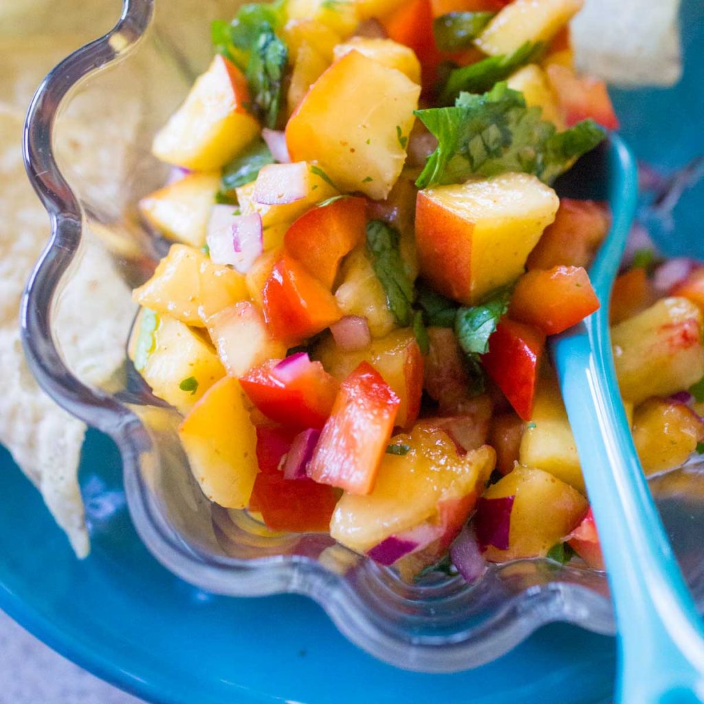 A fresh peach salsa with cilantro sits next to some tortilla chips.
