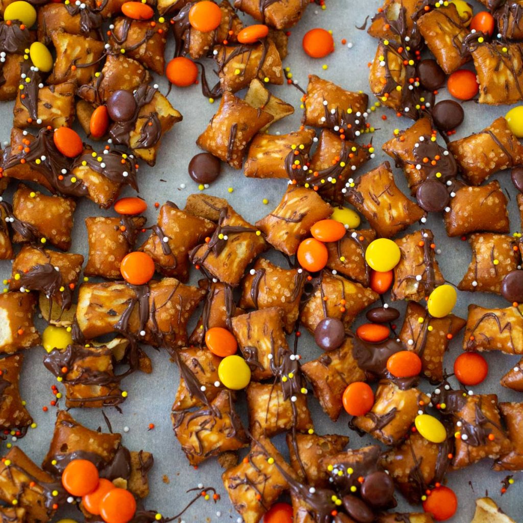 chocolate drizzled peanut butter filled pretzel nugges have orange and yellow candies mixed in.