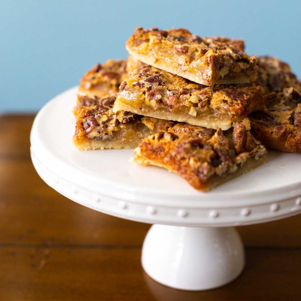 A stack of pecan pie bars on a cake plate.