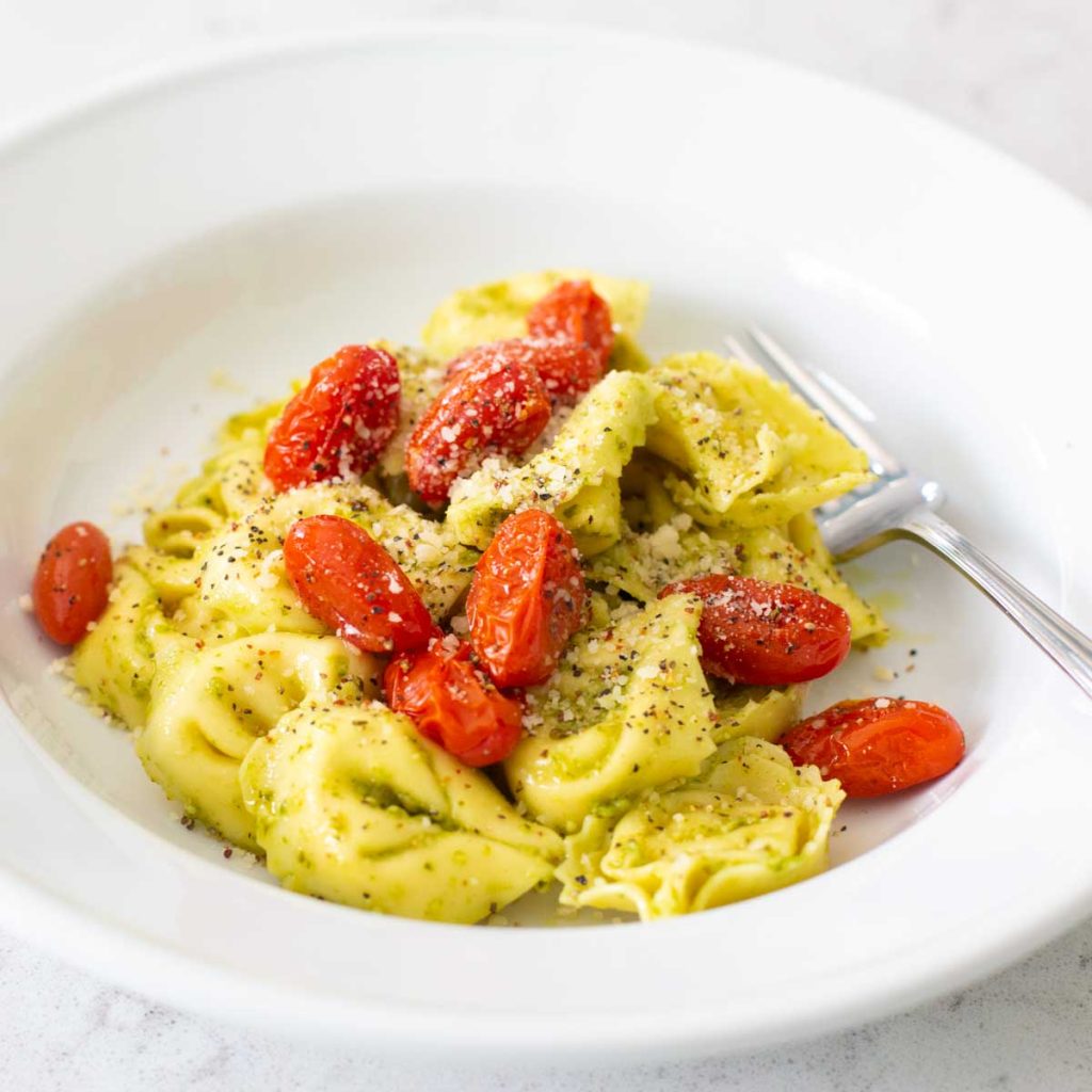 A bowl of cheese tortellini with pesto and cherry tomatoes.