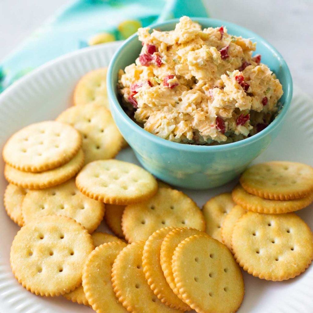 A bowl of pimento cheese spread with butter crackers on a plate.