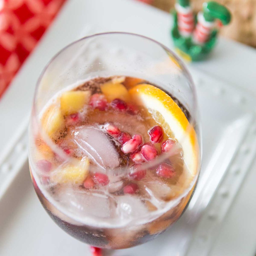 A pomegranate cocktail with fresh citrus and ice in a stemless wine glass.