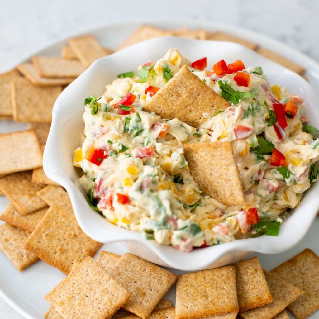 A white bowl has a creamy vegetable dip with Wheat Thins.
