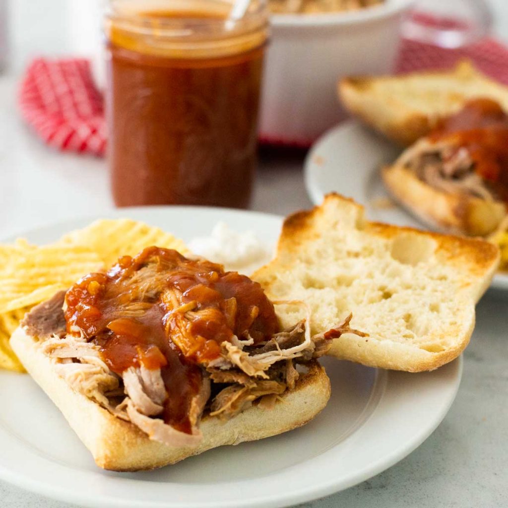A ciabatta roll has a pile of pulled pork with bbq sauce drizzled over the top.