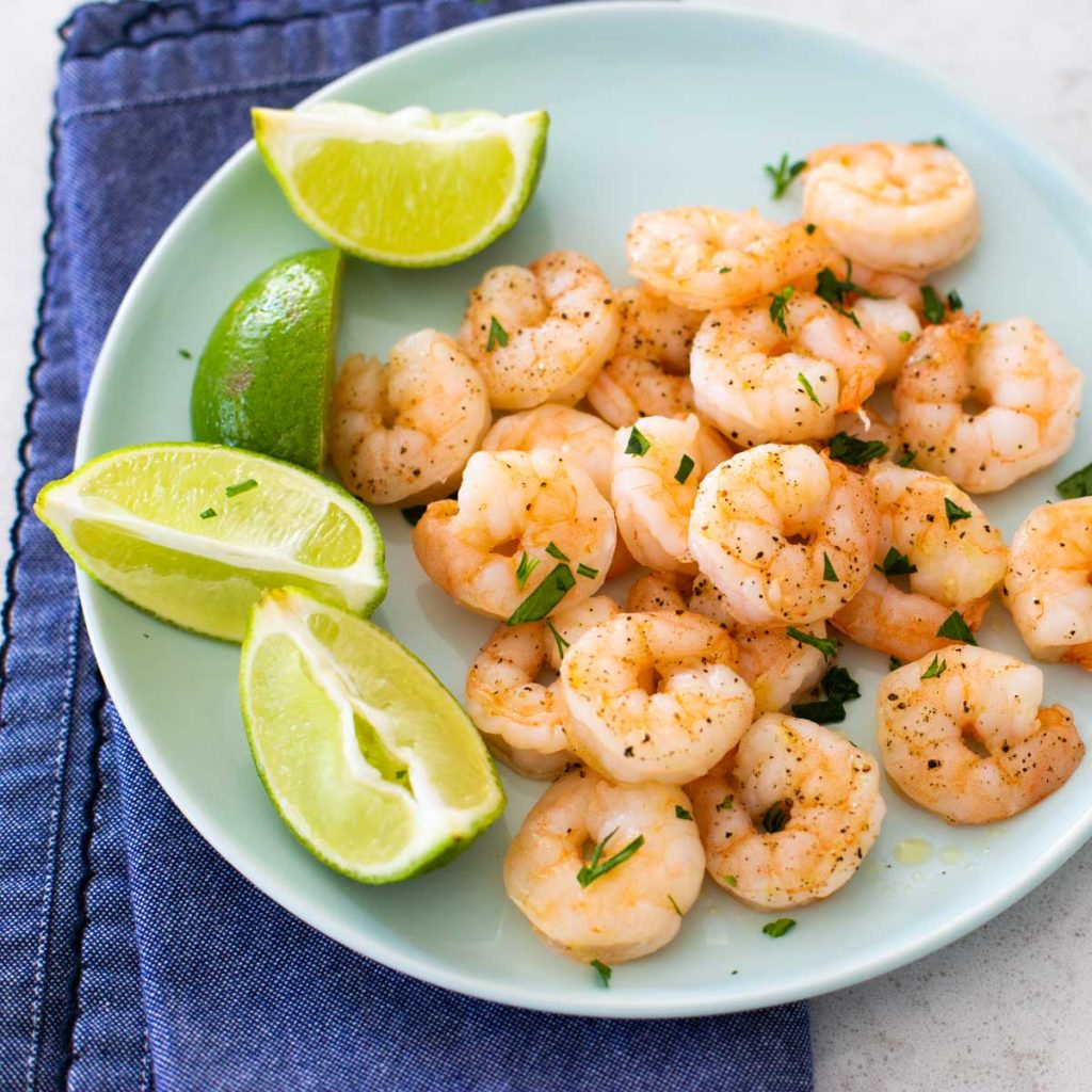 A blue plate with roasted shrimp and lime wedges.