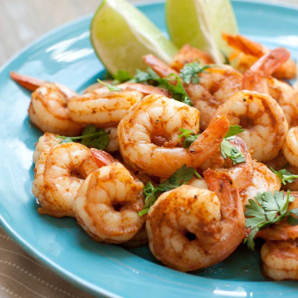 A blue plate with spicy shrimp and fresh lime wedges.