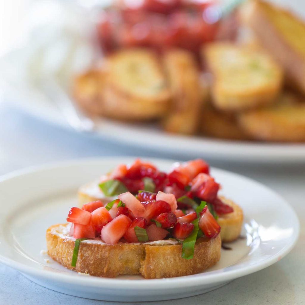 A crostini with fresh strawberry salsa with basil is on a white plate.