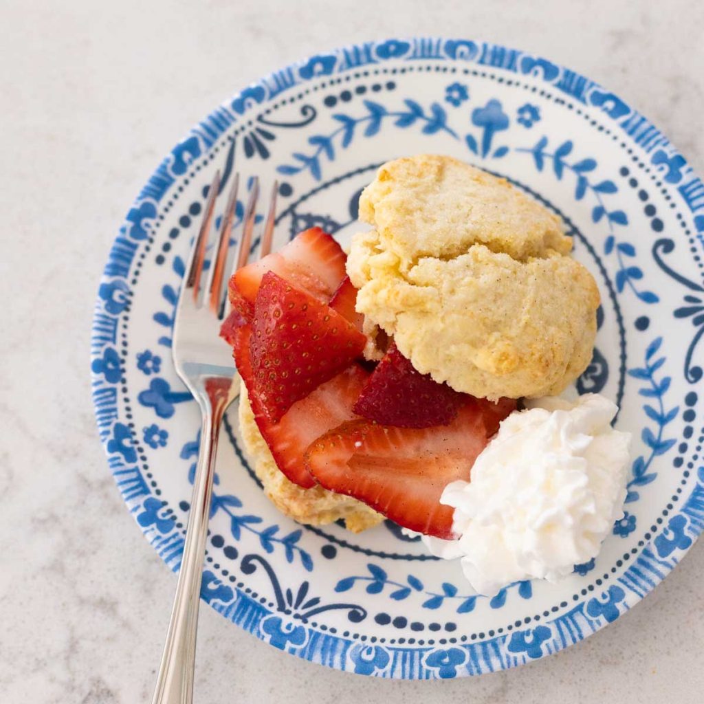 A strawberry shortcake with whipped cream is on a blue plate with a fork.