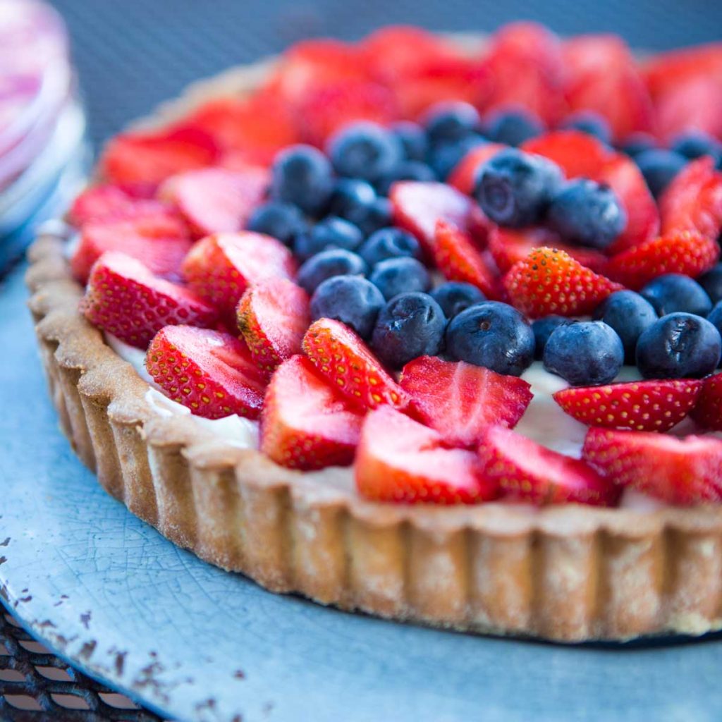 A pretty fresh strawberry and blueberry tart sits on a blue plate.