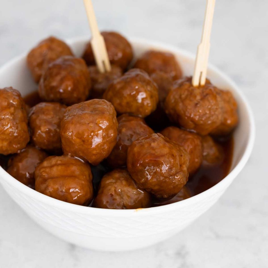 A white bowl of sweet and sour meatballs with party picks.