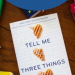 A copy of the book Tell Me Three Things is on the table.