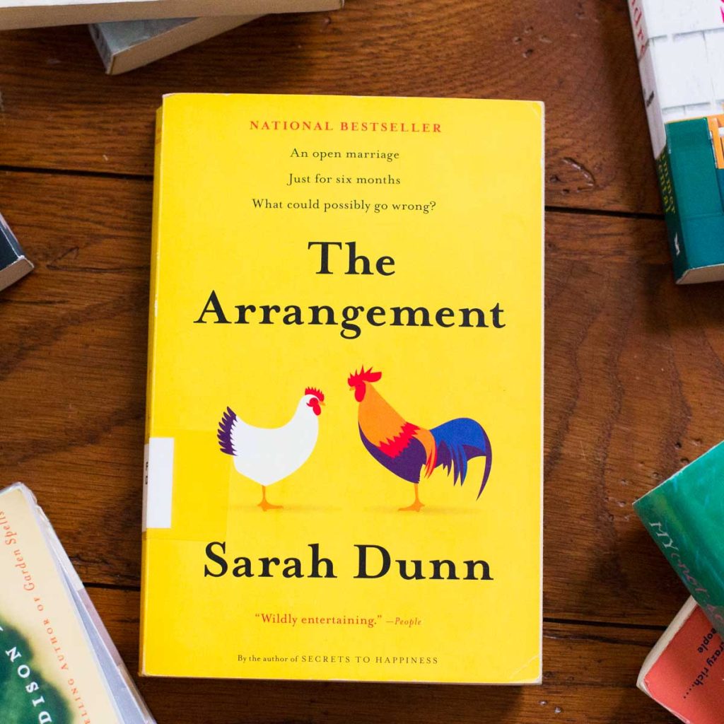 A copy of the book The Arrangement is on the table.