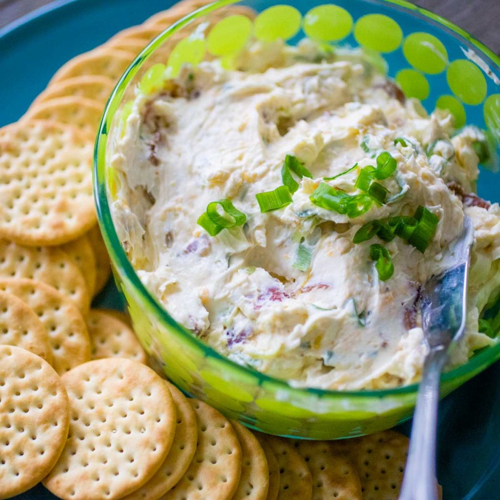 A bowl of creamy cheese dip has butter crackers on the plate next to it.