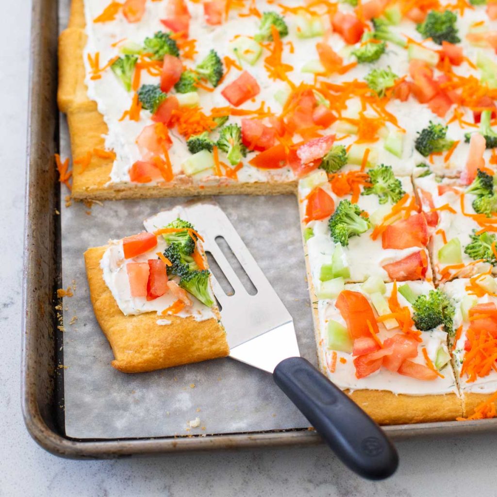 A crescent roll crust topped with cream cheese and chopped raw veggies to make a veggie pizza.