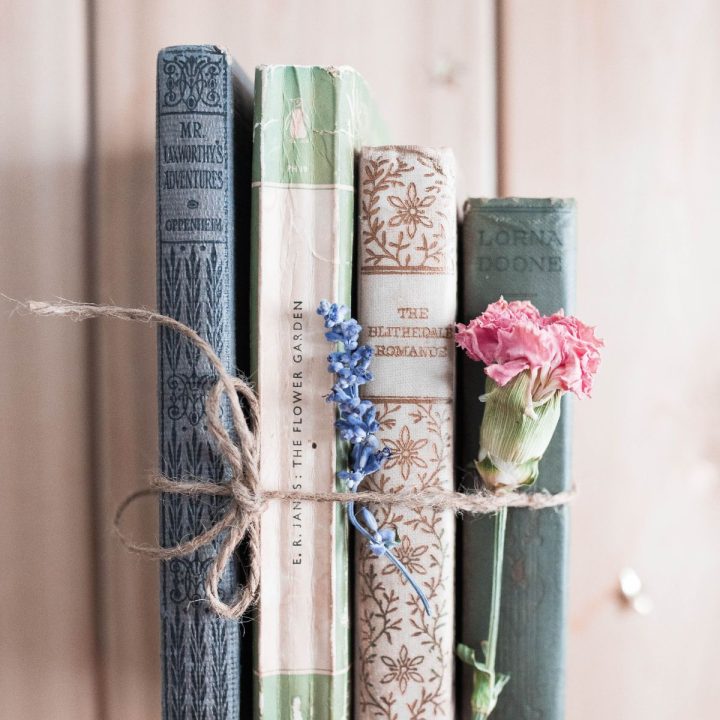 A stack of books tied with twine has a pink carnation tucked inside.